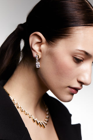 Image of a model wearing the Phenom Emerald Drop Earrings and coordinating necklace shot from the side with her head tilted down. 